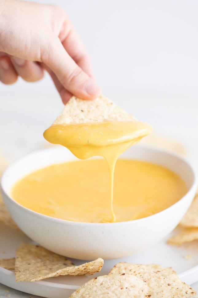 Mano mojando un nacho en un bol de queso vegano de patata