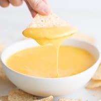 Foto pequeña de una mano mojando un nacho en un bol de queso vegano