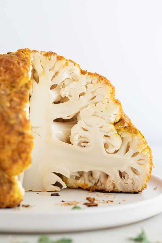 Foto de perfil de una cabeza de coliflor asada y troceada sobre un plato