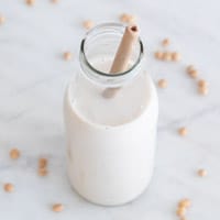 Foto cuadrada de una botella con leche de soja y una pajita dentro