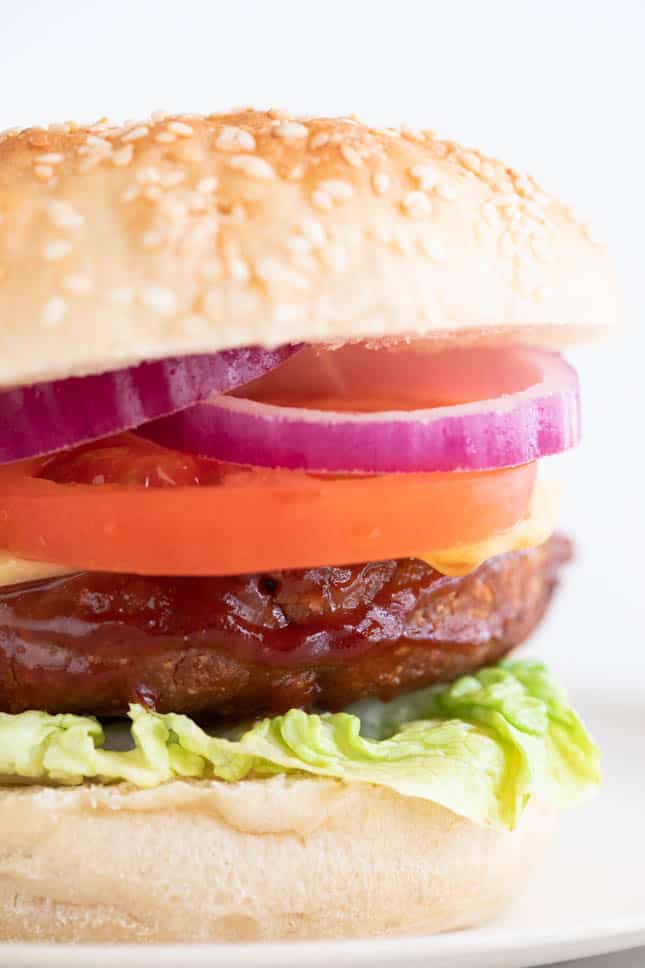 Foto de cerca de un plato con una hamburguesa vegana con lechuga, queso, tomate y cebolla morada