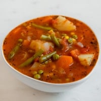 Foto cuadrada de un bol blanco con sopa de verduras