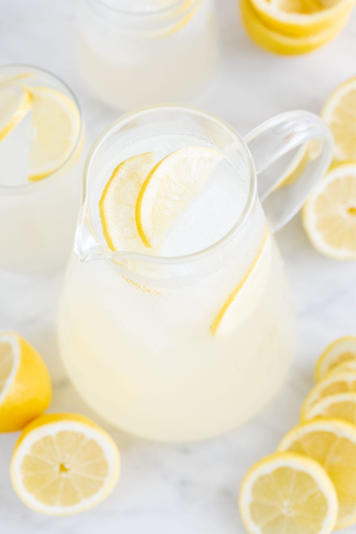 Jarra de limonada casera con un par de vasos y limones alrededor.