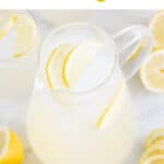 Jarra de limonada casera acompañada de vasos y rodajas de limón como decoración.