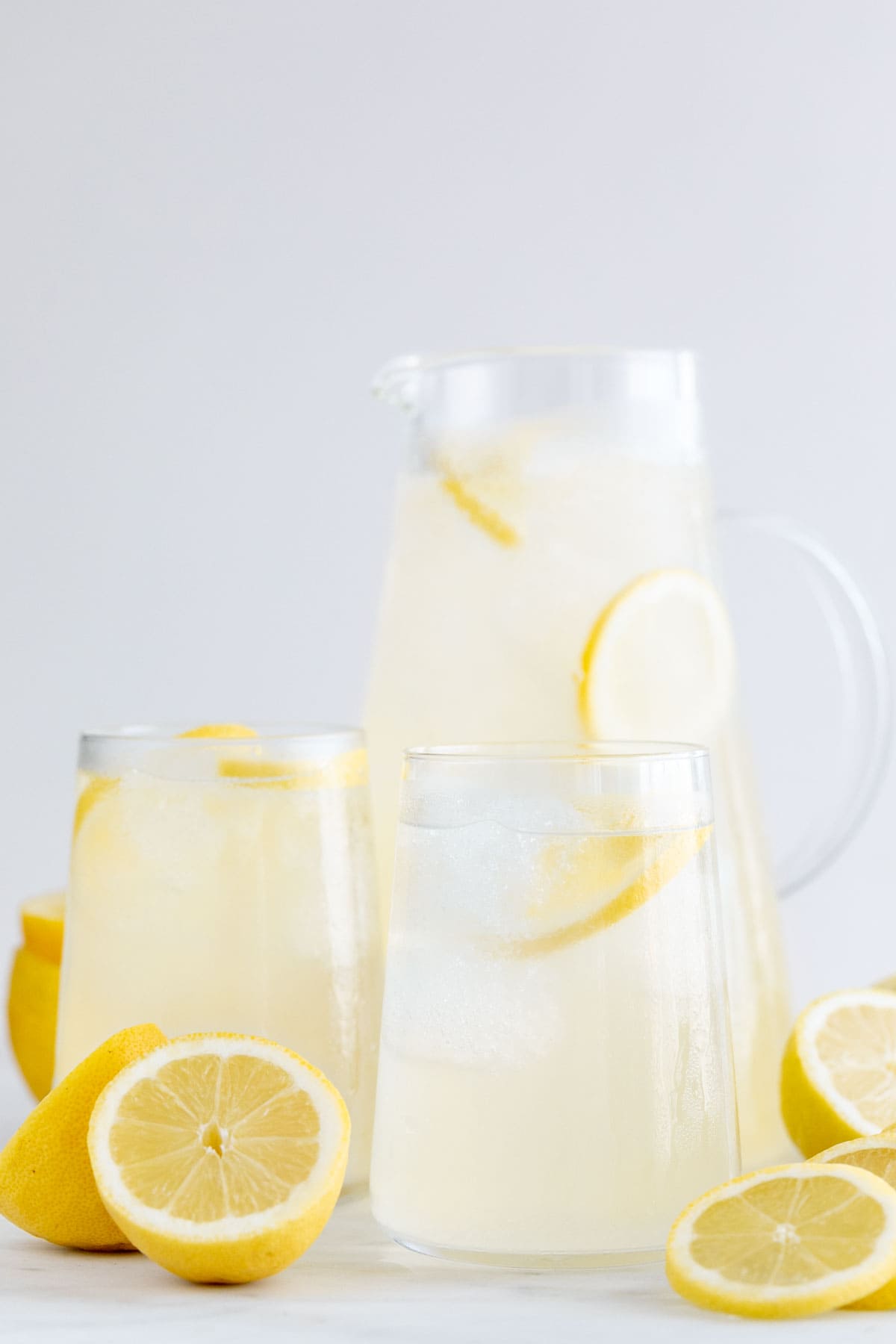 Jarra y vasos con limonada casera y limones alrededor.