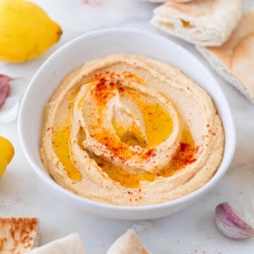 Bol de hummus adornado con aceite de oliva, pimentón y acompañado de pan de pita.
