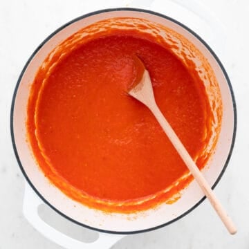 Olla con salsa de tomate y una cuchara de madera sumergida en ella.