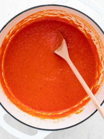 Olla con salsa de tomate y una cuchara de madera sumergida en ella.