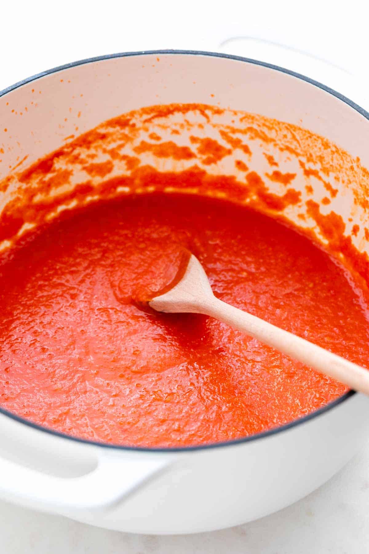 Olla blanca con salsa de tomate y una cuchara dentro.