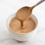 Cuchara vertiendo tahini en un bol.
