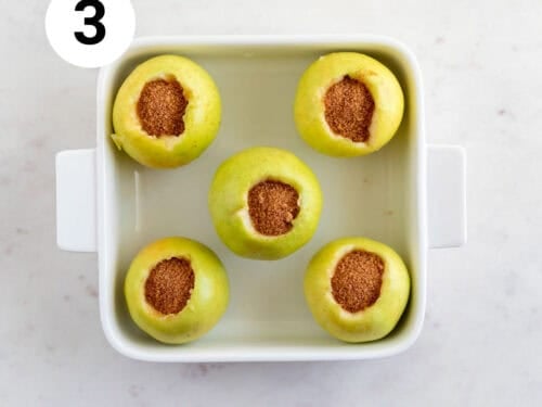 Manzanas descorazonadas con la mezcla de azúcar y canela dentro en una fuente para horno.