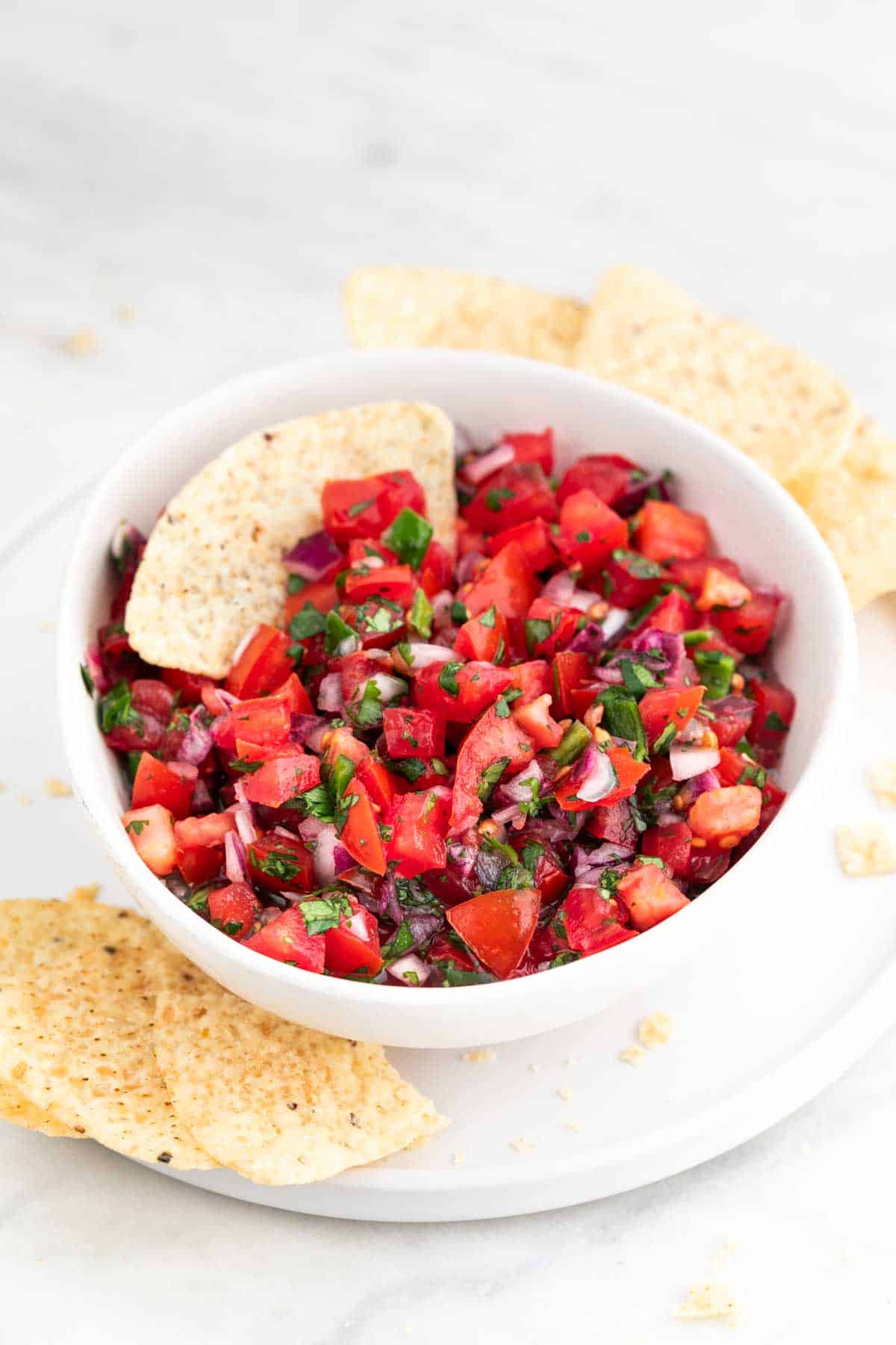 Bol de salsa pico de gallo en plato blanco con nachos alrededor.