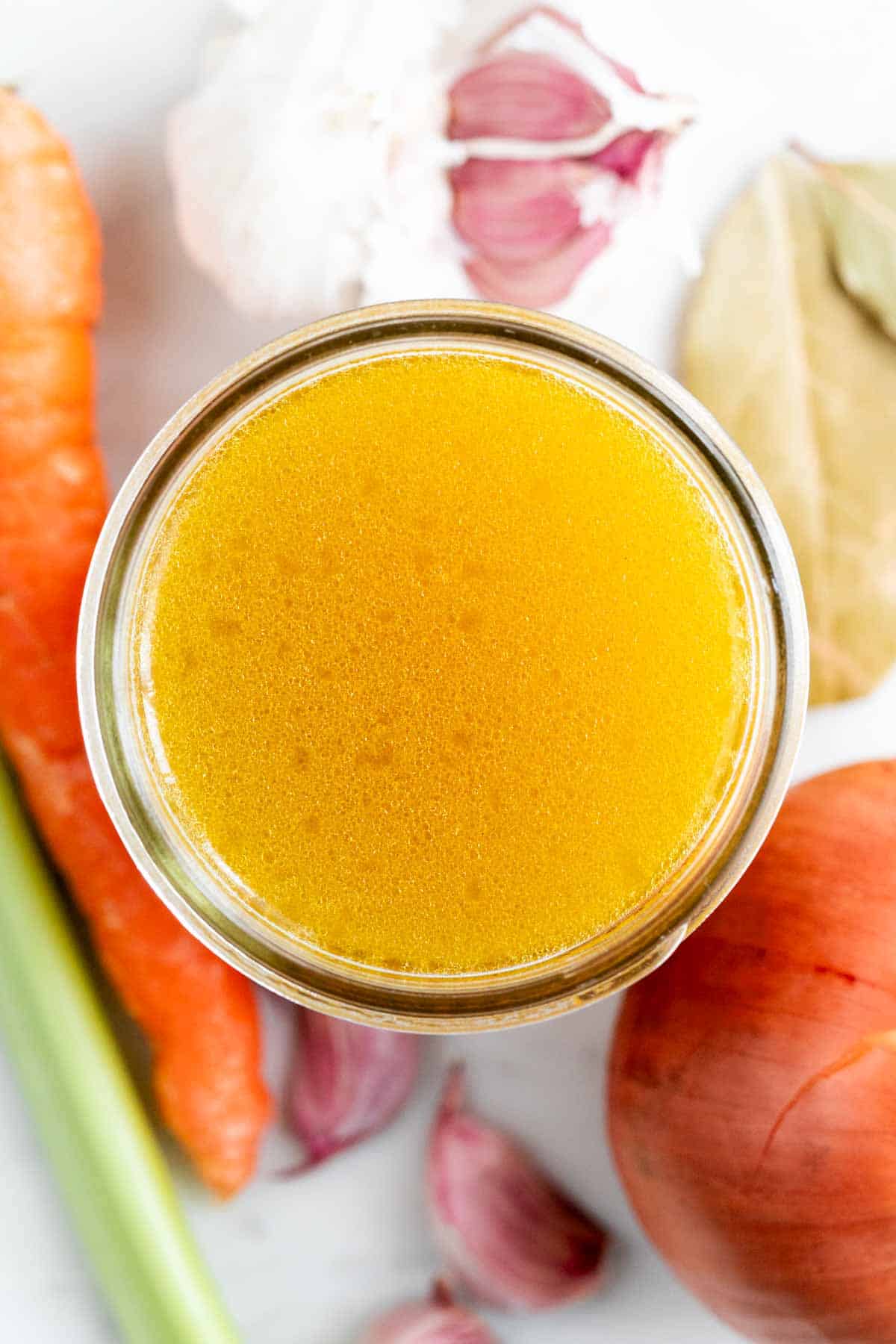 Caldo de verduras casero en un tarro con verduras alrededor.