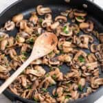 Sartén con champiñones al ajillo y un cuchara.