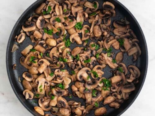 Champiñones al ajillo cocinados en una sartén.