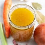 Tarro de caldo de verduras con verduras alrededor.