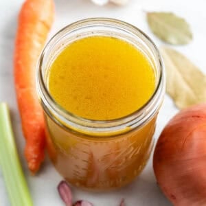 Tarro de caldo de verduras con verduras alrededor.