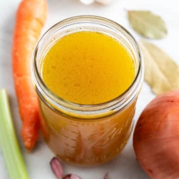 Tarro de caldo de verduras con verduras alrededor.