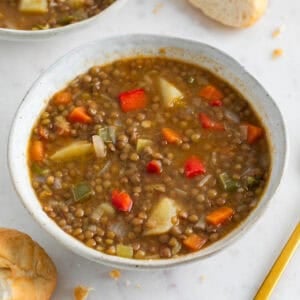 Dos boles de lentejas con verduras con pan de fondo.