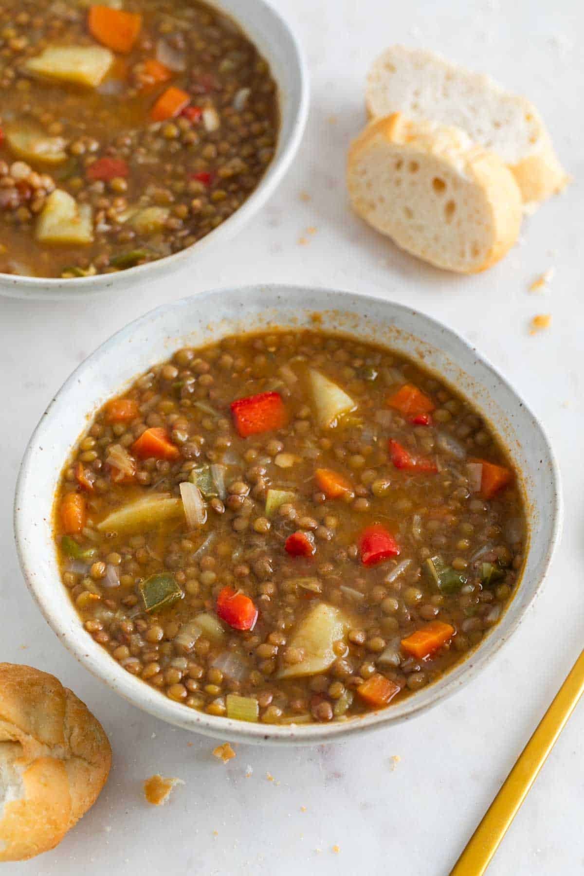 Dos boles de lentejas con verduras con pan de fondo.