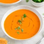 Dos boles con sopa de tomate decorados y un bol con albahaca y pan al fondo.