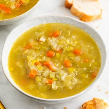 Dos platos de sopa de verduras con pan al fondo.