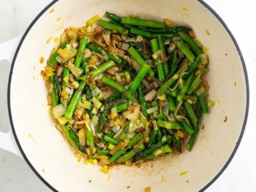 Cebolla. puerro y espárragos salteados en una olla.
