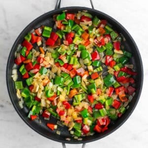 Sartén con cebolla, ajo y pimientos cocinados.