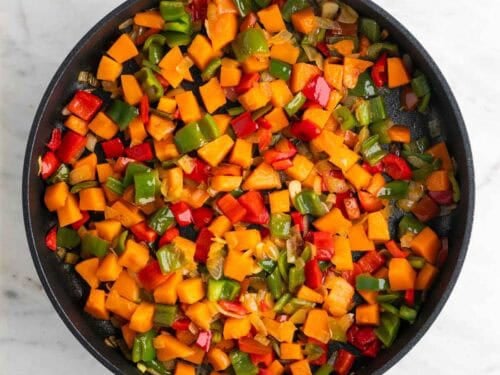 Sartén con cebolla, ajo, pimientos y calabaza cocinados.