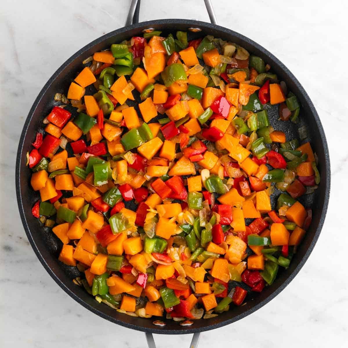 Sartén con cebolla, ajo, pimientos y calabaza cocinados.