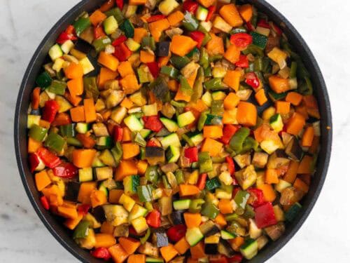 Sartén con cebolla, ajo, pimientos, calabaza, berenjena y calabacín cocinados.