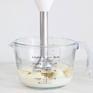 Ingredientes para hacer alioli con leche en una jarra con una batidora de mano.