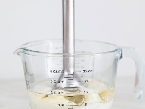 Ingredientes para hacer alioli con leche en una jarra con una batidora de mano.