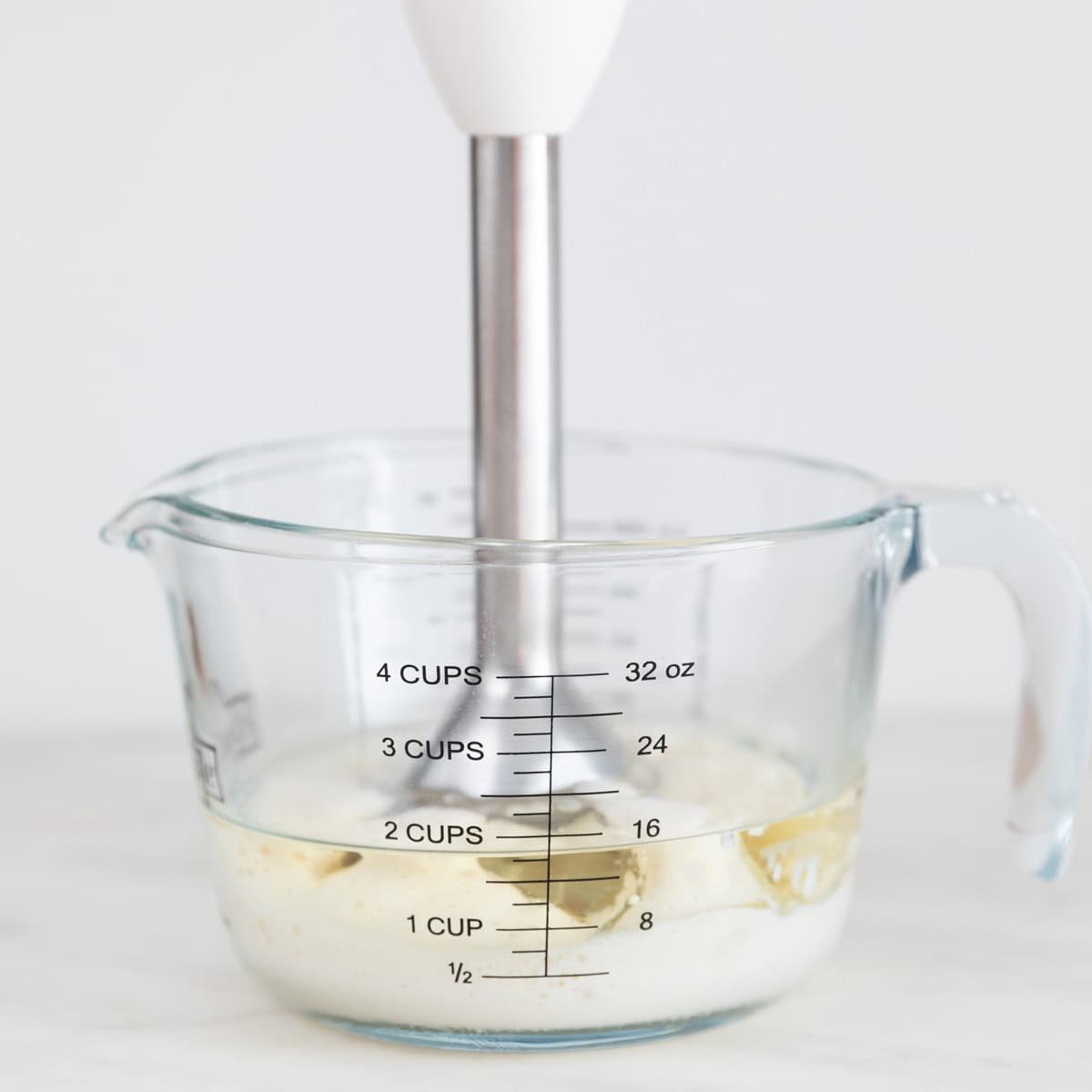 Ingredientes para hacer alioli con leche en una jarra con una batidora de mano.