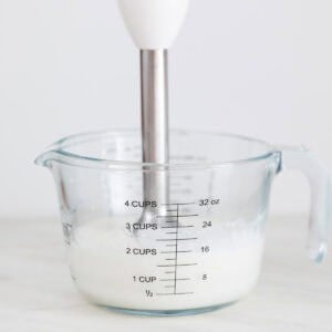 Alioli con leche en una jarra con una batidora de mano dentro.