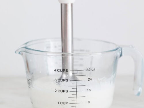 Alioli con leche en una jarra con una batidora de mano dentro.