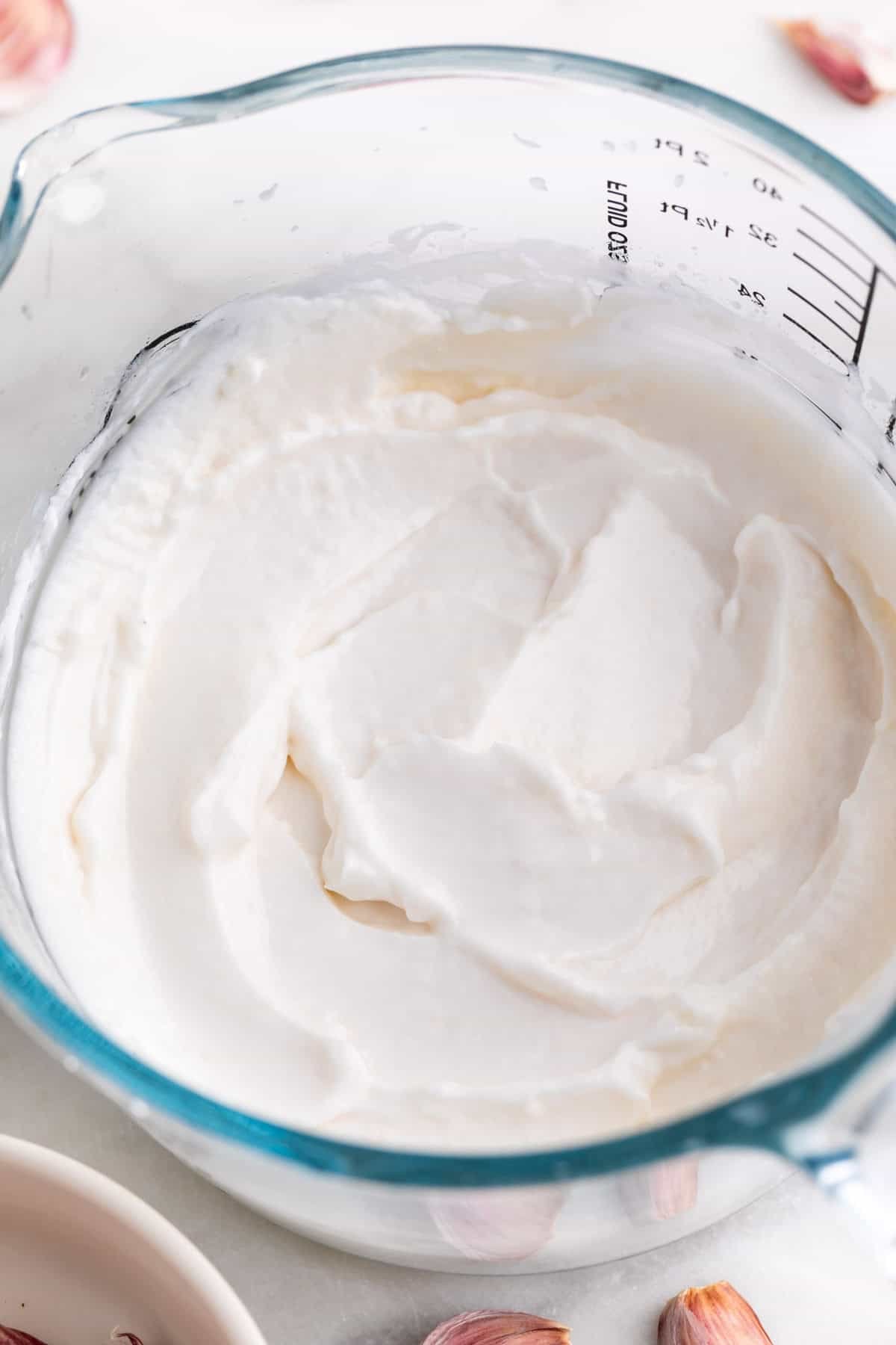 Jarra de alioli con leche con ajos alrededor.