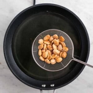 Espumadera con almendras fritas sobre una sartén con aceite.