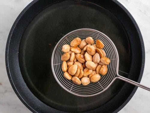 Espumadera con almendras fritas sobre una sartén con aceite.