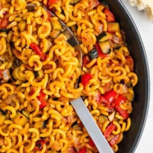 Paellera con fideuá de verduras y pan de fondo.