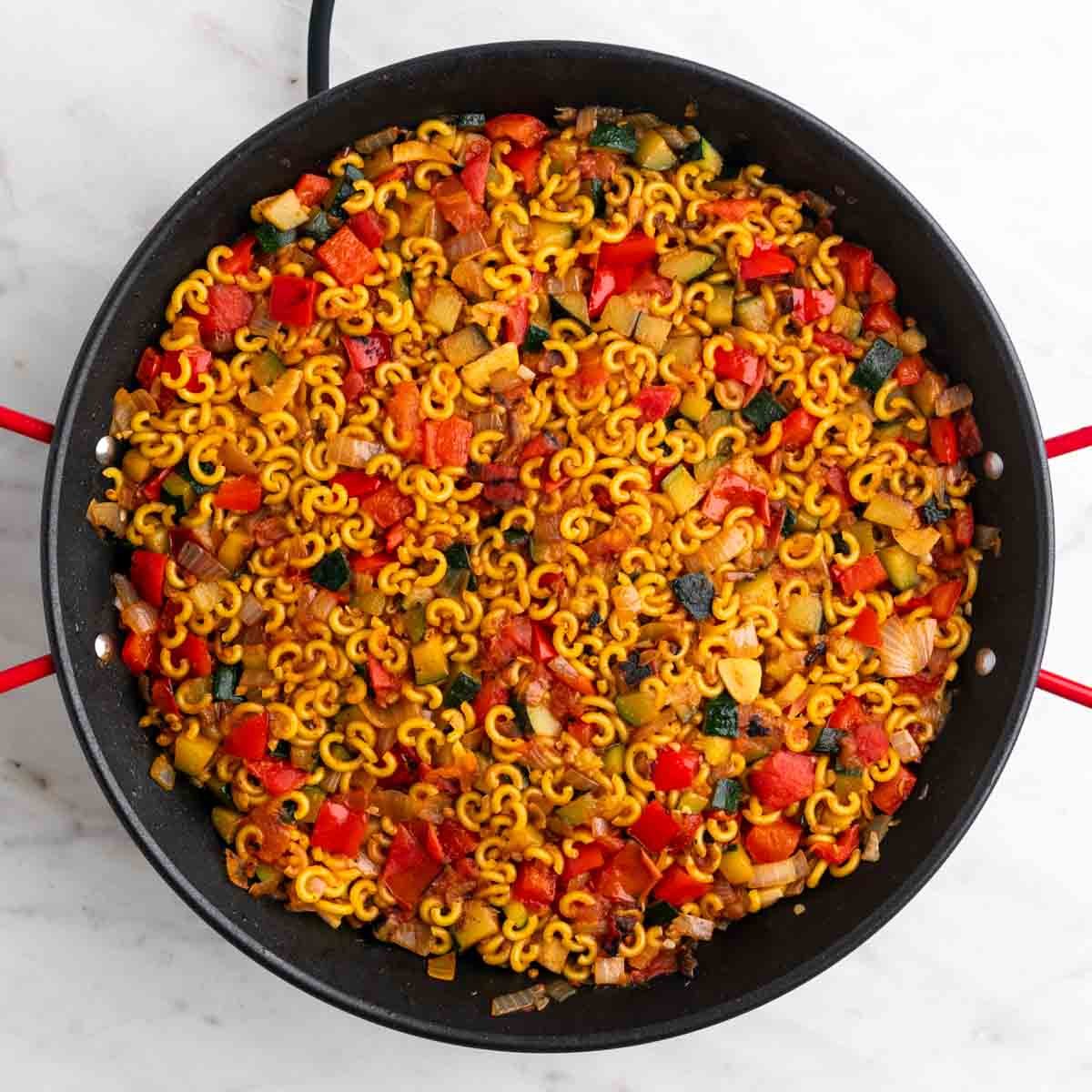 Fideos antes de cocinarse con sofrito de verduras en una paellera.
