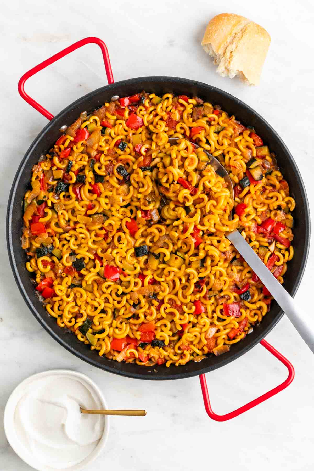 Paellera con fideuá de verduras y alioli y pan de fondo.
