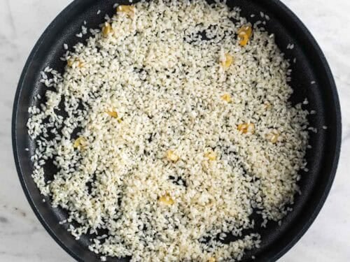 Arroz crudo salteado con ajo en una sartén.