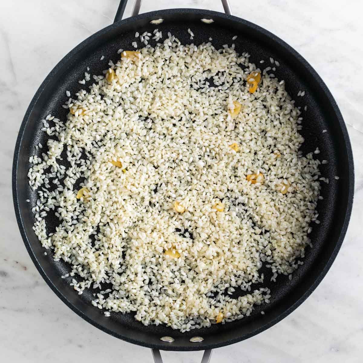 Arroz crudo salteado con ajo en una sartén.