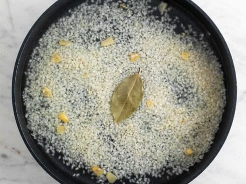 Arroz con ajo, laurel y agua en una sartén antes de cocinarse.