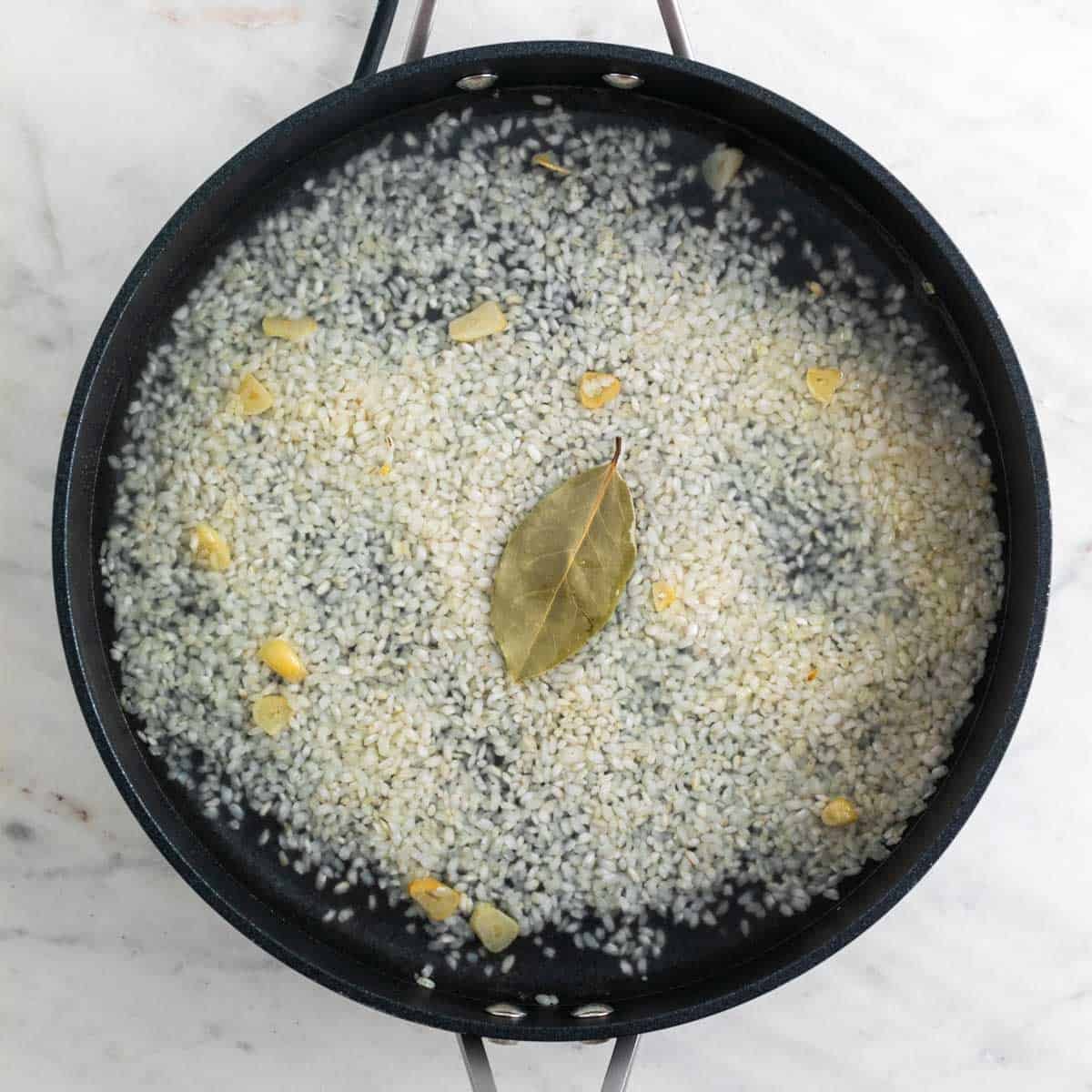 Arroz con ajo, laurel y agua en una sartén antes de cocinarse.