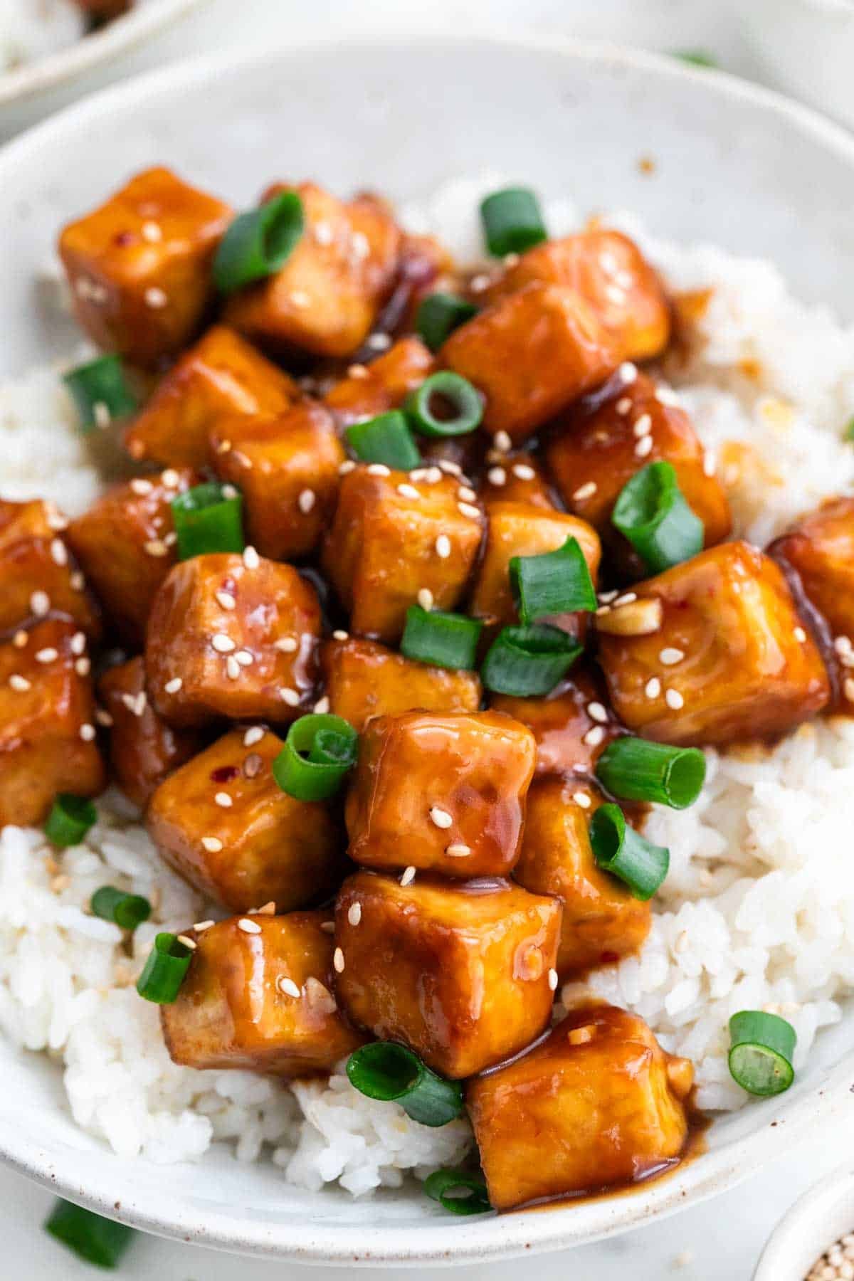 Plato con arroz y tofu a la naranja decorado con sésamo y cebolleta.