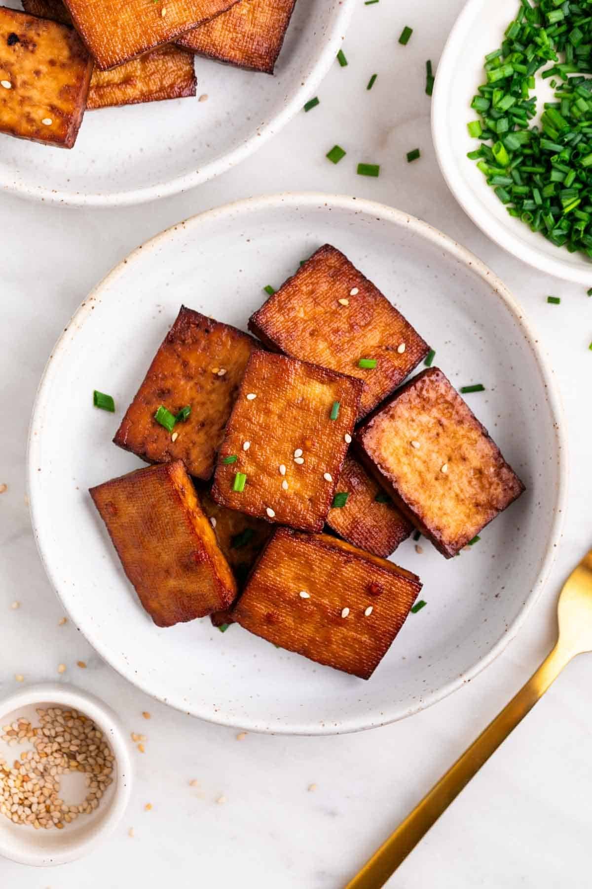 Tofu ahumado en un plato decorado con sésamo y cebollino.