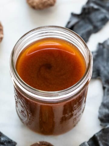 Tarro de salsa de pescado vegana, rodeado de setas shiitake y alga deshidratada.