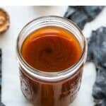 Salsa de pescado vegana en un frasco de cristal, con ingredientes al fondo.